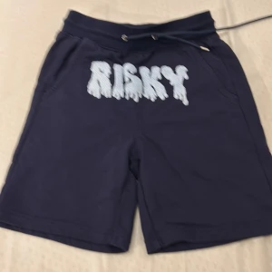 Mörkblå shorts från Risky - Snygga mörkblå shorts från Risky med ett coolt tryck på framsidan. De har snörning i midjan för justerbar passform och är perfekta för en avslappnad stil.