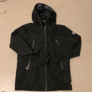 Svart jacka från Moncler - Snygg svart jacka från Moncler med huva och dragkedja. Jackan har flera praktiska fickor med dragkedjor och en stilren design. Perfekt för kyligare dagar.