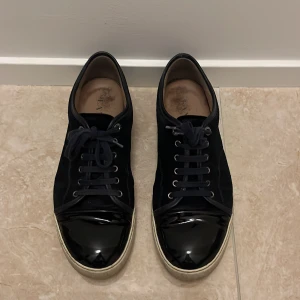 Svarta sneakers från Lanvin - Snygga svarta sneakers från Lanvin med glansig tå och snörning. Skorna har en stilren design med en kontrasterande vit sula. Perfekta för en trendig look. 