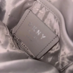 Grå quiltad axelväska från DKNY - Snygg grå axelväska från DKNY med quiltad design och kedjedetaljer på axelremmen. Perfekt för att ge en stilren touch till din outfit.