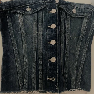 Jeanskorsett från Zara - Snygg jeanskorsett från Zara med knappar framtill och fransig nederkant. Den har en cool vintage-look med detaljerade sömmar och en elastisk del bak för bättre passform aldrig använt.I storleken m men passar s den är  liten i stoleken🩷