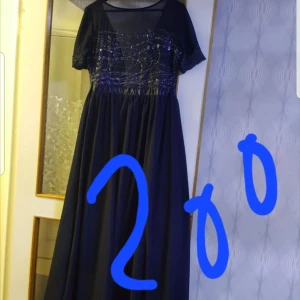Svart långklänning med paljetter - Elegant svart långklänning med glittriga paljettdetaljer på överdelen. Klänningen har korta ärmar och en flytande kjol som ger en vacker silhuett. 40/42