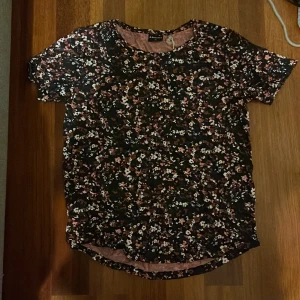 Blommig t-shirt från Firefly - Säljer en blommig tröja från Firefly i svart med rosa och vita blommor. T-shirten har en rund halsringning. Perfekt för en avslappnad stil. Köpt för 149 kr från Intersport, oanvänd.