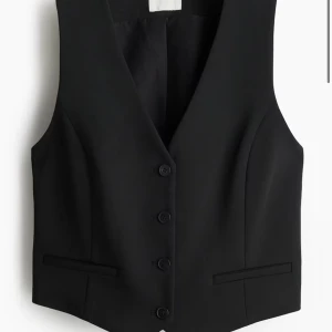 Svart kostymväst med knappar - Snygg svart kostym väst med knappar framtill. Perfekt för en stilren look. Västen har en klassisk design med en v-ringad hals och två fickor. 