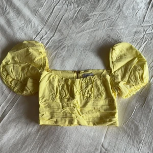 Gul croppad topp från Oh Polly -  söt gul croppad topp från Oh Polly med puffiga korta ärmar och dragkedja bak.  Strl small