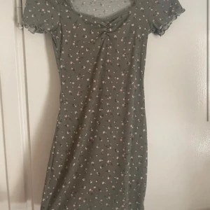 Grön blommig klänning från H&M Divided - Söt grön klänning med små blommor från H&M Divided. Klänningen har korta ärmar och en rundad halsringning med en liten knutdetalj framtill. Perfekt för en avslappnad stil.