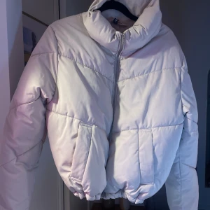 Ljusgrå pufferjacka med dragkedja - Säljer en snygg ljusgrå pufferjacka från H&M Jackan har en hög krage och praktiska fickor framtill. Perfekt för kyliga dagar.