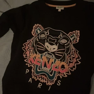 Svart tröja med tigerbroderi från Kenzo - Snygg svart tröja från Kenzo med ett färgglatt tigerbroderi och texten 'Kenzo Paris' på framsidan. Perfekt för en stilren look med en touch av attityd.