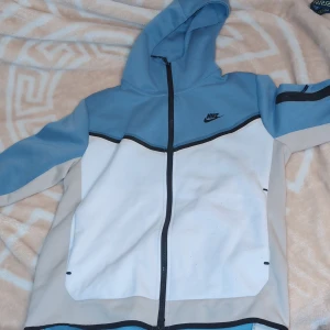 Blå och vit jacka från Nike Med dragkedja  - Snygg blå och vit jacka från Nike med dragkedja och huva. Perfekt för kyligare dagar med sin sportiga look och bekväma passform. PRISET KAN DISKUTERAS 