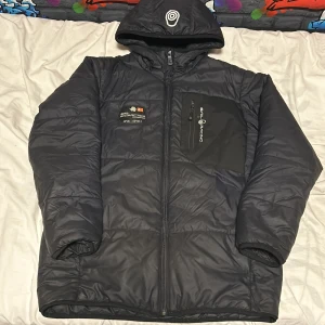 Svart dunjacka från Sail Racing - Säljer en svart dunjacka från Sail Racing med huva och dragkedja. Jackan har en cool 'Antarctica Expedition'-detalj på bröstet och en logotyp på huvan. Perfekt för kalla dagar äkta storlek 160 