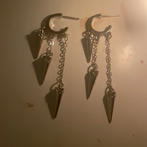 Silvriga örhängen med kedjor och spetsar - Snygga silvriga örhängen med kedjor och spetsformade hängen. Perfekta för att ge en edgy touch till din stil. De har en modern design med flera hängande delar som skapar rörelse.