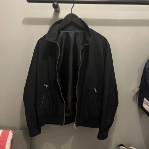 Svart Limitato jacka med tryck - Snygg midnight blue Limitato jacka med dragkedja och ett stort tryck på ryggen. Jackan har ribbade muddar och en krage, vilket ger en klassisk look. Perfekt för en stilren och modern outfit.