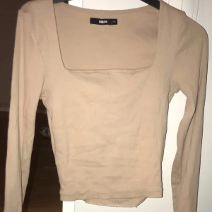 Beige ribbad topp från Bik Bok - Säljer en stilren beige ribbad topp från Bik Bok. Toppen har en fyrkantig halsringning och långa ärmar, perfekt för en chic vardagslook. Passar bra till både jeans och kjol.