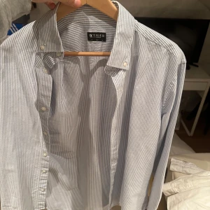 Randig skjorta från Tiger of Sweden - Snygg randig skjorta från Tiger of Sweden i blått och vitt. Skjortan har en klassisk krage och knappar framtill. Perfekt för en stilren look.