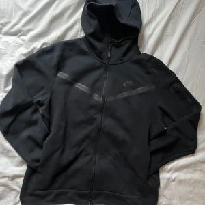 Svart Nike Tech Fleece från Nike - Säljer en svart hoodie från Nike med dragkedja och huva. Den har en diskret logga på bröstet och är tillverkad i ett mjukt material. Nypris 1499:-