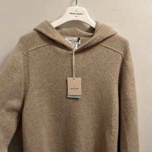 Gran Sasso hoodie - Säljer en stilren beige hoodie från Gran Sasso. Tröjan är tillverkad i ett mjukt material och har långa ärmar med ribbade muddar. Perfekt för en avslappnad look. Hör av dig vid intresse!