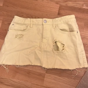 Gul kjol från Lindex - Säljer en cool gul kjol från Lindex med slitna detaljer och rå kant. Kjolen har en klassisk femficksdesign och är perfekt för en avslappnad stil. Den är gjord i ett bekvämt material och har en knapp och dragkedja framtill.