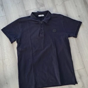 Mörkblå pikétröja från Moncler - Snygg svart pikétröja från Moncler i bomull. Tröjan har en klassisk krage med knappar och Monclers logotyp broderad på bröstet. Perfekt för en stilren look.