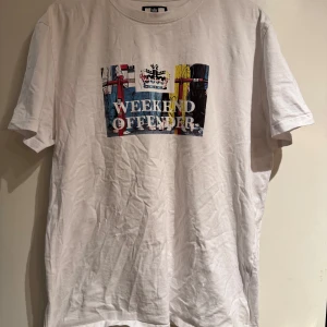 Vit t-shirt från Weekend Offender - Säljer en vit t-shirt från Weekend Offender med tryck och texten 'Weekend Offender' på framsidan. Perfekt för en avslappnad stil. Storlek L. Väldigt lite använd! Nypris 499kr 