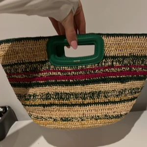 Randig handväska från Maje handgjord ❤️❤️ - Säljer en snygg handväska från Maje i randigt mönster med gröna, röda och beige färger. Väskan har ett grönt handtag och är perfekt för en somrig look. Den är tillverkad i ett flätat material som ger en naturlig känsla.handgjord 