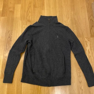 Grå ralph lauren zip merino ull - Säljer en stilren grå kofta från Polo Ralph Lauren. Inga defekter. Koftan har en dragkedja framtill och är tillverkad i ett mjukt material. Perfekt för kyligare dagar med sin klassiska design och långa ärmar. Materialet är merino ull. Nypris ca 2,5 k