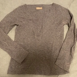 Grå kashmirtröja från Zadig & Voltaire - Säljer en elegant grå kashmirtröja från Zadig & Voltaire. Tröjan har en v-ringad design och långa ärmar, perfekt för en stilren look. Tillverkad i 100% kashmir för en lyxig och mjuk känsla. Passar utmärkt för kyligare dagar.