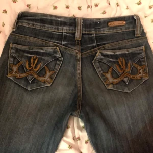 Blå jeans med broderade bakfickor - Assnygga jeans från 90/00 talet!!!! Lågmidjade och med broderade fickor, passar till de mesta! Passar någon längre då de är rätt så långa byxor (kanske passar någon runt 170cm+), är liiittee långa på mig som är 168 men de funkar fortfarande! Skriv om ni har några frågor eller vill ha några mått 💗💗💗