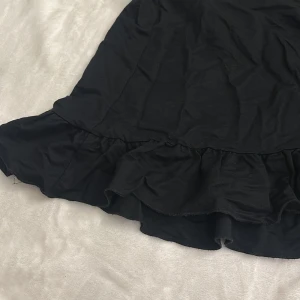 Svart kjol med volang - Snygg svart kjol med volangdetaljer i nederkant. Perfekt för att ge en elegant touch till din outfit. Kjolen har en klassisk passform och är lätt att matcha med olika toppar. Storlek M men passar s också
