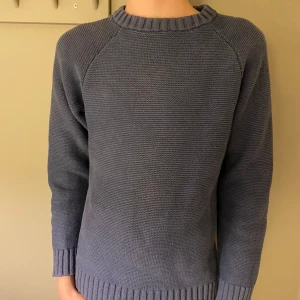 Blå stickad tröja - Säljer en stilren blå stickad tröja med långa ärmar och ribbade muddar vid ärmslut och nederkant. Perfekt för kyligare dagar.