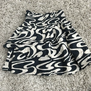Svartvit kjol från H&M - Säljer en cool svartvit kjol från H&M med ett unikt mönster. Kjolen har en elastisk midja för bekväm passform och en volangdetalj som ger extra stil. Perfekt för att sticka ut i mängden!