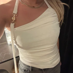 Vit oneshoulder topp - Snygg vit oneshoulder topp med en unik design och justerbara banddetaljer. Perfekt för en stilren look.