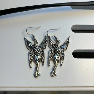 Silverfärgade älvörhängen - Charmiga örhängen i form av älvor med detaljerade vingar. De är silverfärgade och har en krok för enkel användning. Perfekta för att ge en magisk touch till din stil. Pris kan diskuteras🩷