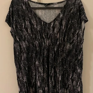 Blusar från Gina Tricot - Snygg blusan från Gina Tricot med ett unikt mönster i svart och grått. Klänningen har en v-ringad hals och korta ärmar, perfekt för en stilren look. Materialet är mjukt och bekvämt, vilket gör den lätt att bära hela dagen.