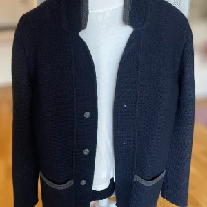 Dark Blue Blaser I M - Snygg och elegant stickad kavaj i mörkblå färg. Kavajen har en fin struktur och detaljer i grått. Den har en klassisk krage, knappar framtill och fickor. Perfekt för både vardag och festligare tillfällen.