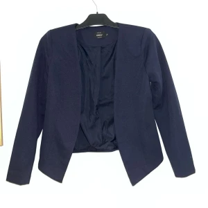 Mörkblå kavaj från Only - Snygg mörkblå kavaj från Only i en stilren design. Kavajen har en öppen front utan knappar och långa ärmar. Perfekt för att ha över en klänning eller till en lite festligare outfit! 