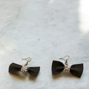 Svarta örhängen med rosett och glittrig detalj - Snygga svarta örhängen i konstläder, formade som rosetter med en glittrig detalj i mitten. Perfekta för att ge en elegant touch till din outfit.