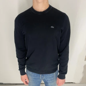 Svart tröja från Lacoste - Säljer en stilren svart tröja från Lacoste med rund halsringning och det svarta krokodilmärket på bröstet. Fint skick, inga fel. Det står storlek M men passar som S. Modellen är 173cm och väger 65kg. 