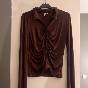 Brun och vit topp från Nelly - Säljer två snygga toppar från Nelly i storlek M. Den ena är brun och den andra vit, båda med långa ärmar och en snygg rynkad detalj framtill. Perfekta för att ge din outfit det lilla extra! Den vita är aldrig använd därav prislappen medans den bruna är testad en gång, tyvärr rykt bort prislappen på den! Ny pris 400