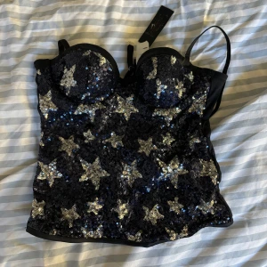 Svart paljettkorsett med stjärnor - Snygg svart korsett topp täckt med glittriga paljetter i form av stjärnor. Perfekt för en kväll ute eller en festlig tillställning. Från intimissimi i storlek S aldrig använd endast testad.