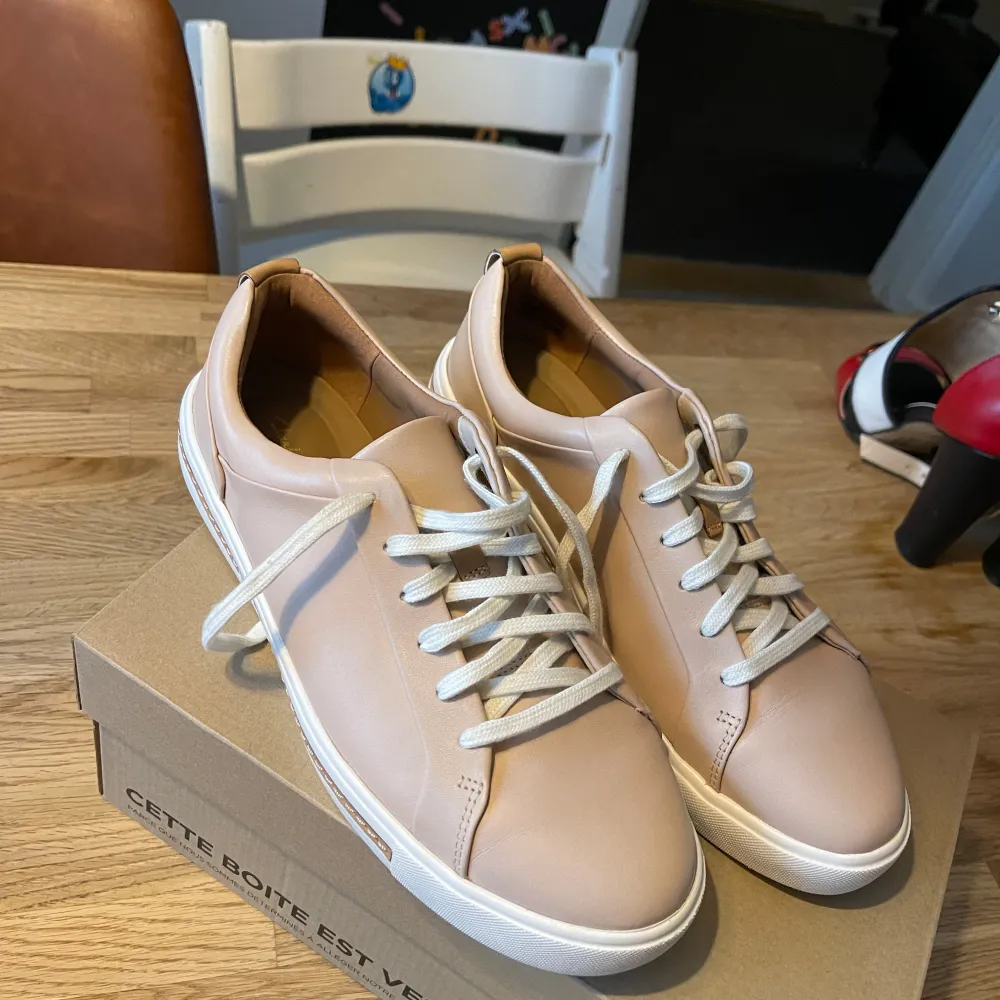 Snygga beige-ros sneakers från Clarks med vit sula och snörning. Perfekta för en stilren look. Skorna har en enkel och modern design som passar till många olika outfits.Helt nya med kartong . Kengät.