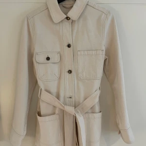 Beige jacka från & Other Stories - Snygg beigevit jacka från & Other Stories med knappar och knytskärp i midjan. Nypris 2200, aldrig använd!!