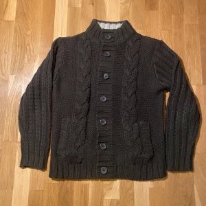 Unik stickad cardigan - Säljer en mysig mörkbrun stickad kofta med knappar framtill och flätstickade detaljer. Koftan har en hög krage med ribbad kant i kontrasterande färg. Perfekt för kyliga dagar! Ifall mer frågor eller bilder så skriv gärna! Mvh