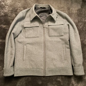 Grå overshirt med dragkedja - Säljer en stilren grå overshirt med dragkedja framtill. Den har två stora bröstfickor och är perfekt nu till höst/vinter. Insidan är fodrad för extra komfort. 1199kr nypris som ni ser på sista bilden. Använd 2-3 gånger så den är som ny!