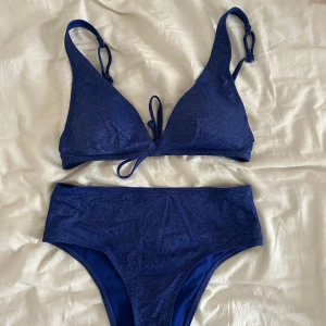 Glittrig bikini  - Oanvänd blå/lila glittrig bikini. Triangel bikini överdel med lite högmidjad underdel. Säljer få den inte kommer till användning 
