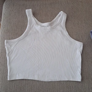 Vit ribbad linnetopp - Säljer en stilren vit ribbad linnetopp i storlek M. Perfekt för sommardagar eller som ett basplagg i garderoben. Toppen är ärmlös och har en croppad passform som ger en modern look.oanvänd. 1000% nytt. 
