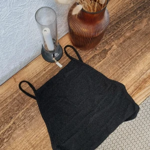 Svart glittrig linne från Gina Tricot - Säljer en snygg svart body från Gina Tricot i storlek S. Det är glittrigt och perfekt för fest. Linnet har smala axelband och en tight passform som ger en stilren look. Passar perfekt till både byxor och kjol!