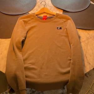 Beige tröja från Nike - Säljer en snygg beige tröja från Nike i storlek S. Den har en liten Nike-logga på bröstet och en praktisk dragkedja på sidan. Perfekt för en casual look eller träning. Tröjan är i bra skick och superbekväm!