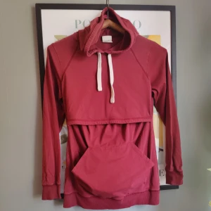 Boobdesign mörkröd hoodie med fleecefodrad amningsfunktion, storlek S - En mörkröd hoodie med fleecefodrad amningsfunktion. Fleece på insidan som håller bysten varm (extra viktigt för dig som ammar). Med ribbade detaljer, flatlocksömmar och en generös känguruficka.