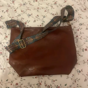 Handväska - Brun handväska, fickor på insidan. Fin axelrem som går att ta bort. Inte använd.