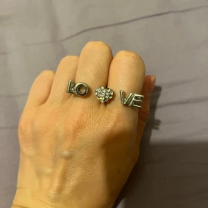 Guldfärgad ring med LOVE-design - Säljer en superfin dubbelring i nyskick som stavar 'LOVE' över två fingrar (Justerbar). Den har en hjärtformad detalj med glittrande stenar i mitten. Perfekt för att ge en extra touch till din outfit! 💖